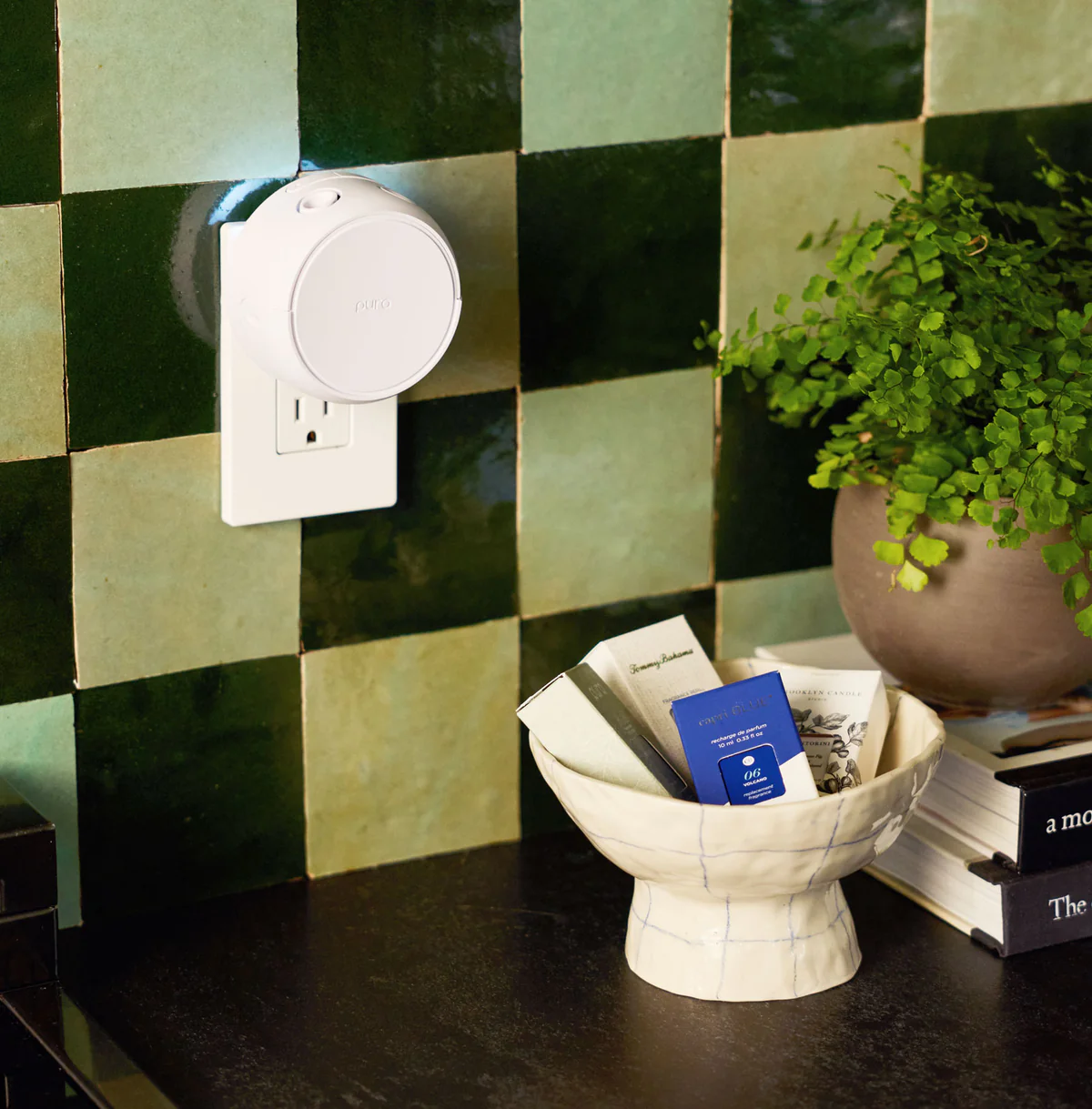 Pura smart diffuser plugged into wall outlet beside fragrance vials in a decorative bowl