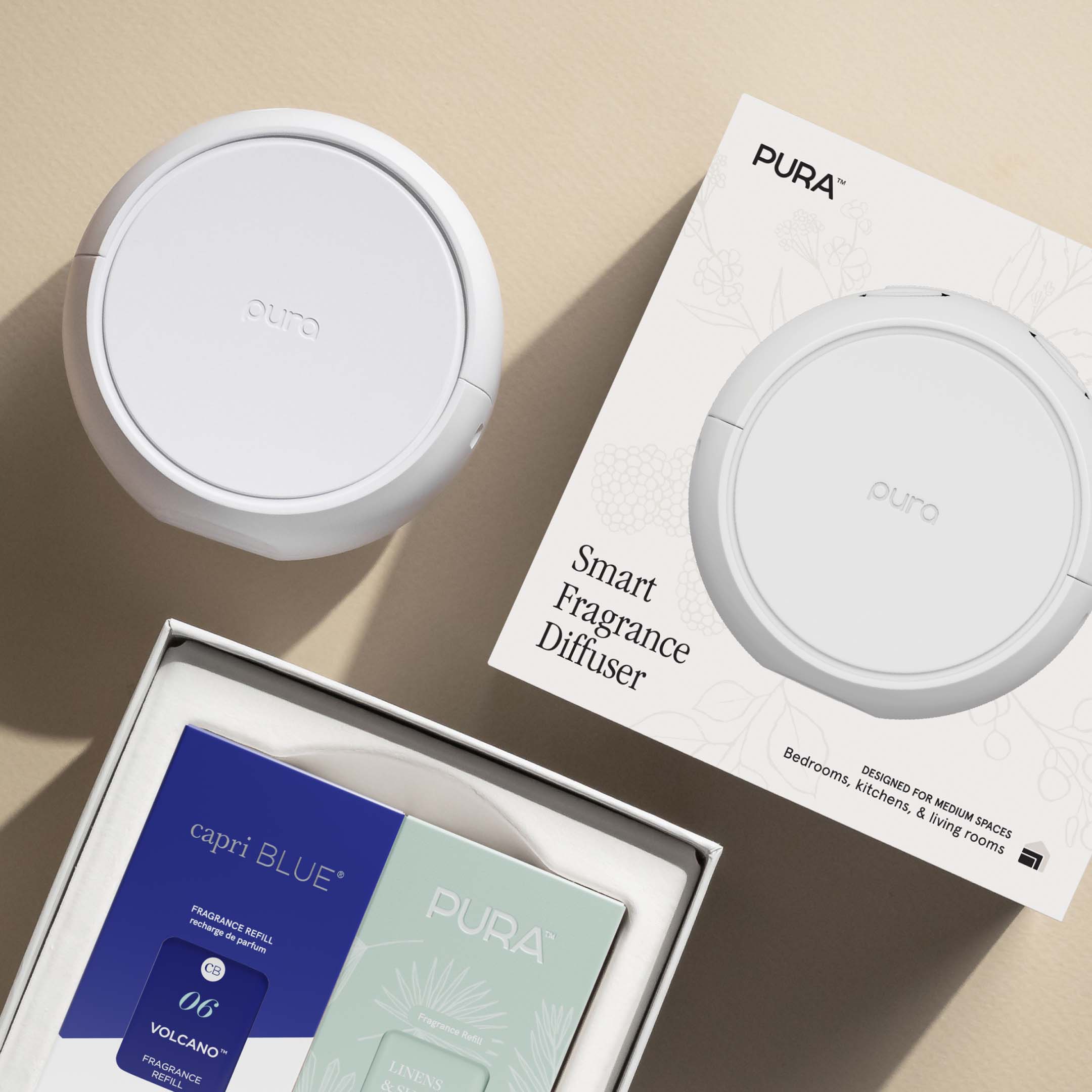 Pura Home smart diffuser and two fragrances in packaging on a beige background