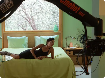 Behind-the-scenes photo of a model relaxing on a bed during Pura's fragrance campaign film shoot, camera crane overhead.