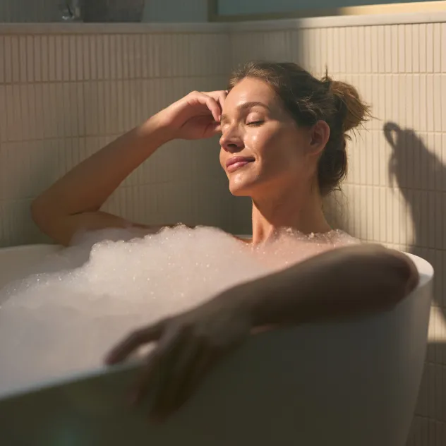 Woman relaxing with her eyes closed in a bubble bath, illuminated by warm sunlight
