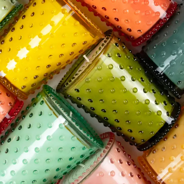 Colorful hobnail glass candle jars in yellow, orange, green, and teal, arranged closely together.