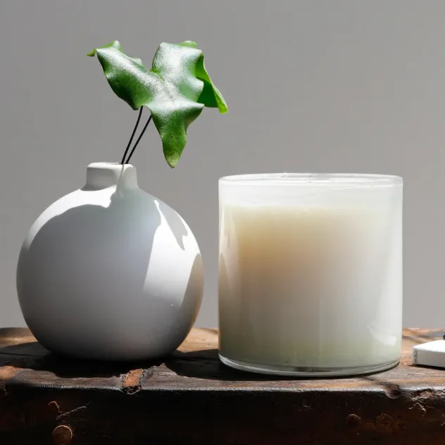 White ceramic bud vase with a green leaf, beside a lit LAFCO candle.