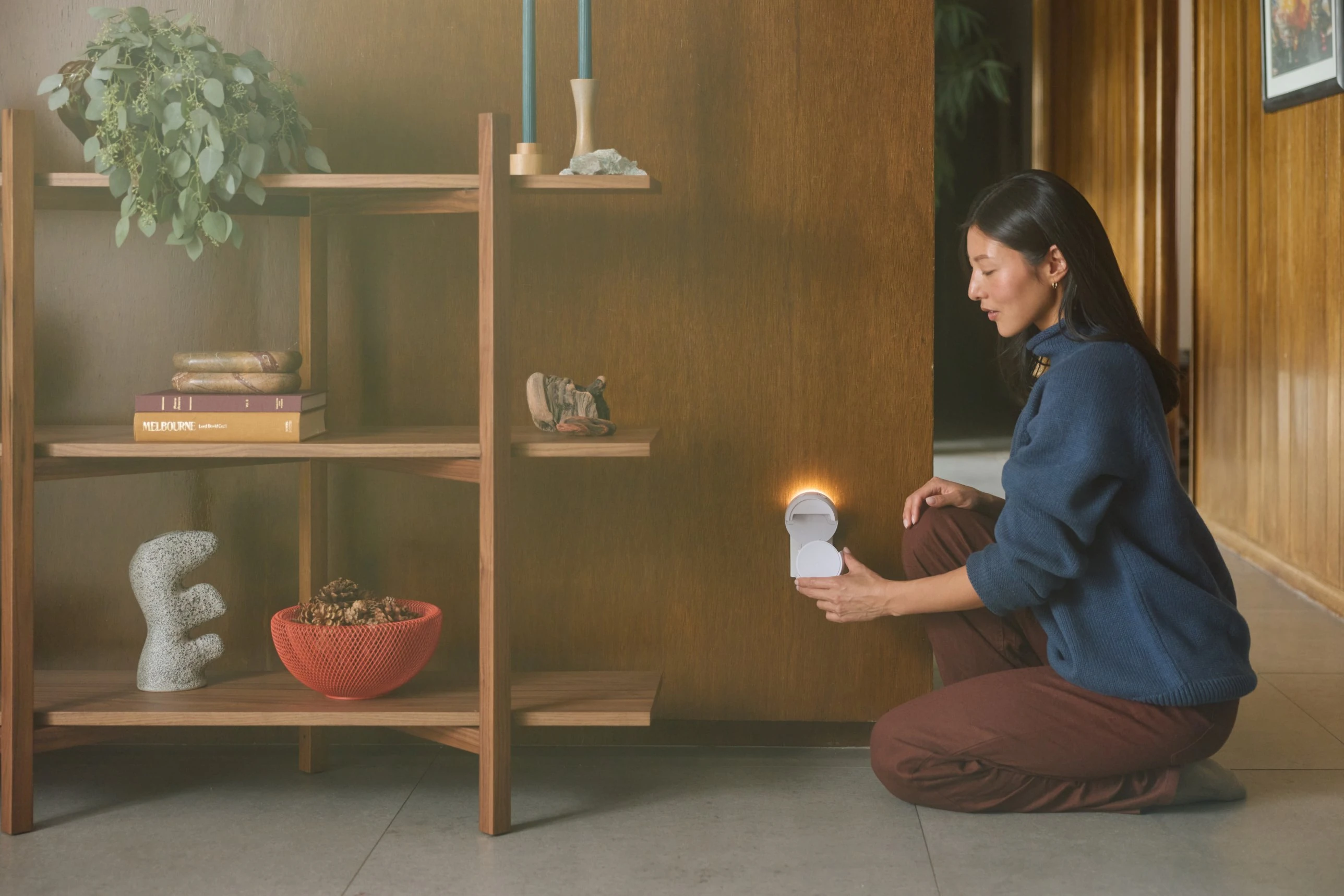 A hand holding a smartphone displaying the Pura app, controlling a smart diffuser with intensity and timer settings