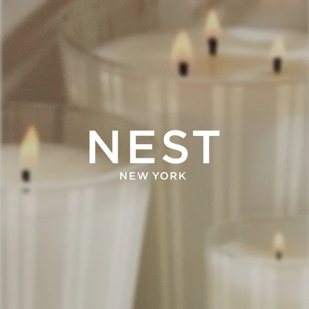 NEST New York logo over three lit white candles in striped glass vessels.